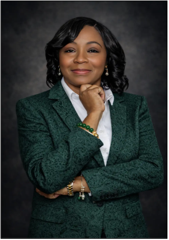 Professional portrait: a woman in a green paisley blazer with a white shirt, resting her chin on her hand and smiling softly.